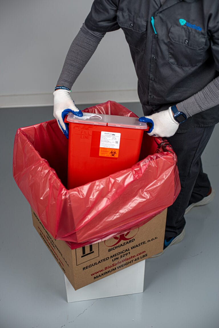 BioSafe technician placing a red sharps container into a lined biohazard waste box