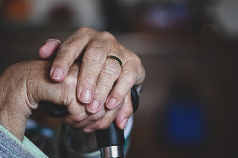 Close-up of an elderly person's hands resting on a walking cane