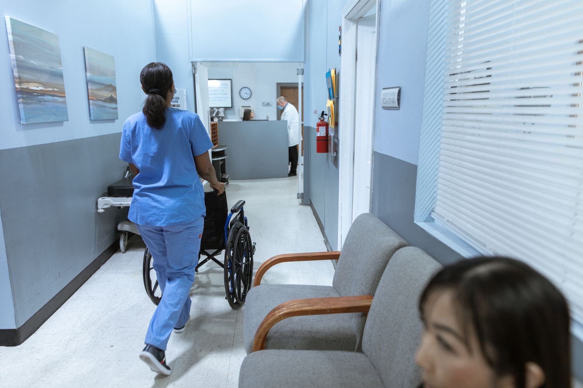 Nurse pushing a wheelchair through a long-term care facility corridor